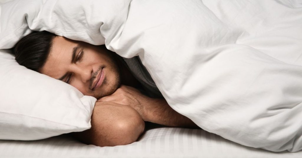 Man curled up in bed under his duvet