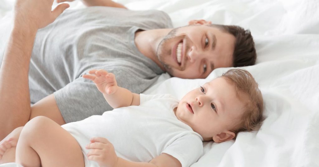 Dad smiling while laying next to his baby on a new organic latex mattress.